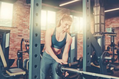Sporcu kadın spor salonunda halter takıyor.