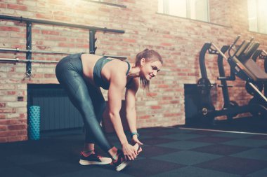 Spor kıyafetleri içinde mükemmel vücudu olan atletik genç bir kadın spor salonunda bacaklarını esnetiyor. Trenden önce ısın.