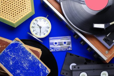 Düz yatay geçmişe dönük özellikler, 80 'lerin medyası. Vinil çalar, video kasetler, ses kasetleri, kayıtlar, radyo, klasik çalar saat, mavi arka plandaki eski kitaplar. Üst görünüm