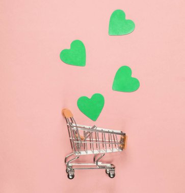 Mini alışveriş arabası, pembe pastel arka planda dekoratif kalpler, üst manzara, minimalizm. Kavramsal fotoğraf
