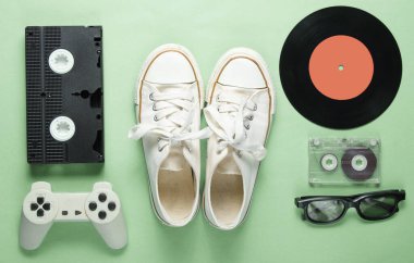 80 'lerden kalma eski moda popüler kültür özellikleri yeşil arka planda. Eski spor ayakkabılar, av alanı, ses kaseti, video kaset, plaka, 3D gözlükler. Minimalizm, üst görünüm