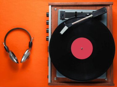Retro vinil plak çalar, turuncu arka planda kulaklıklar. Üst görünüm