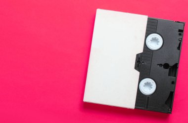 Video cassette in cover, videotape on pink background. Top view, minimalism clipart
