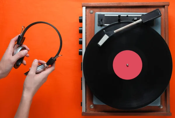 レトロスタイル ビニールレコードプレーヤーと手は ヘッドフォン ミニマリズム オレンジの背景にトップビュー 80年代を保持しています — ストック写真