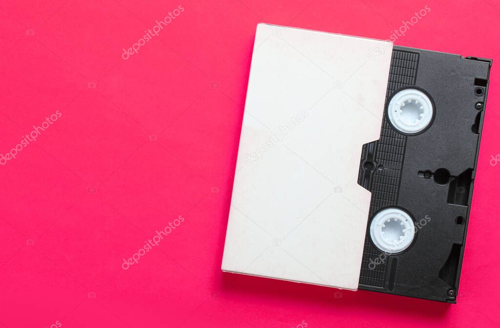 Video cassette in cover, videotape on pink background. Top view, minimalism