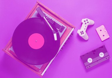 Pembe arka planda düz retro eşyalar vardı. Duotone etkisi. Vinil çalar, video, ses kaseti, oyun alanı. Popüler kültür, 80 'ler. Üst görünüm