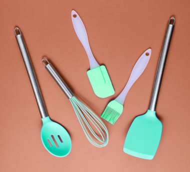 Kahverengi arkaplanda yemek pişirmek için metal saplı silikon araçları