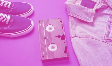 Retro tarzı şeyler. Video kaset, kot ceket, mor arka planda spor ayakkabılar..