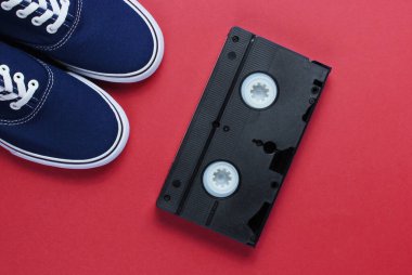 Retro tarzı 80 'ler. Video kaset, kot pantolon, kırmızı arka planda spor ayakkabılar. Üst görünüm