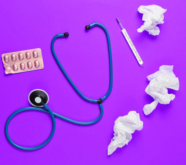 The concept of treating cold diseases. Used nasal wipes, thermometer, pills, stethoscope on purple background. Top view