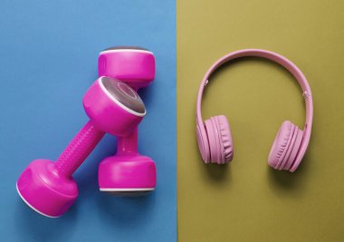 Yaratıcı konsept uygunluğu. Plastik pembe dambıllar, mavi yeşil arka planda kulaklıklar. Minimalizm, üst görünüm, düz uzanma