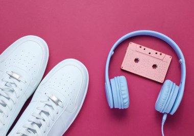 Retro tarzı. 80 'ler. Popüler kültür. Minimalizm. Ses kaseti olan kulaklıklar, kırmızı arka planda beyaz spor ayakkabılar. Üst görünüm
