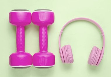 Pembe kulaklıklar, yeşil pastel arka planda plastik halterler. Müzikli spor. Üst görünüm.