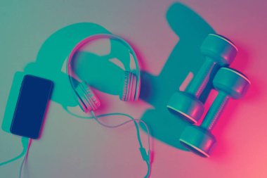 Yaşam tarzı konsepti. Kulaklıklı ve akıllı telefonlu dambıllar. Retro dalga, mavi kırmızı neon ışık, morötesi. Üst görünüm, minimalizm