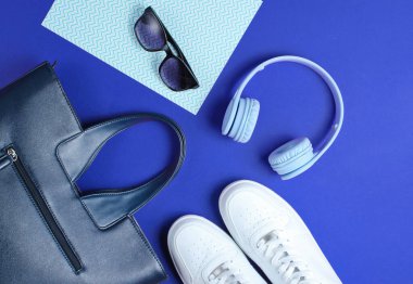 Yaratıcı renk arkaplanı olan modern aksesuarlar. Beyaz spor ayakkabı, deri çanta, kulaklık, güneş gözlüğü. Nesneler. Üst manzara, düz uzanma