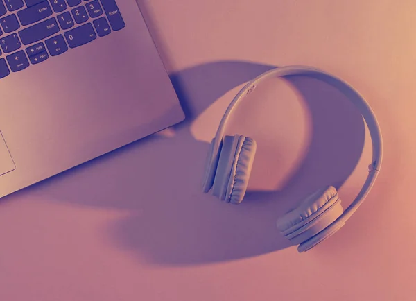 Modern laptop, wireless headphones. Gadgets. Orange purple neon light, ultraviolet. Top view, minimalism