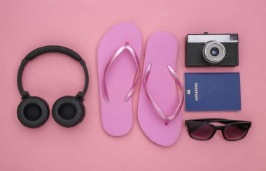 Parmak arası terlikler, kablosuz kulaklıklar, pembe pastel arka planda seyahat aksesuarları. Üst Manzara. Seyahat Düzlüğü