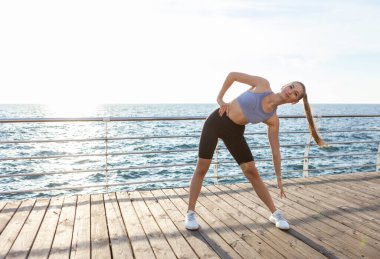 Çekici, zayıf, formda genç bir kadın gün doğumunda plajda ısınma egzersizleri yapıyor.