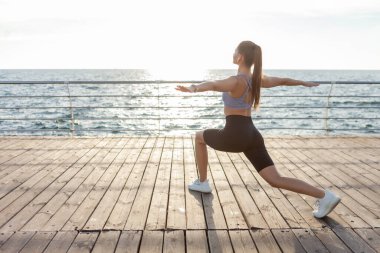 Çekici genç fitness kadını plajda gün doğumunda hatha yoga egzersizi yapıyor.