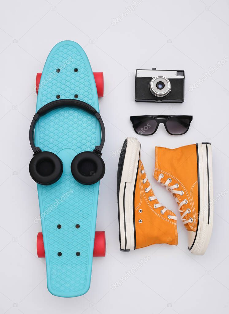 Flat lay composition of youth hipster accessories. Cruiser board, sneakers, headphones, camera and sunglasses on a white background. Top view