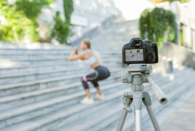 Kameraya odaklan, genç, sarışın, formda, lastik bantlarla merdivenlerde atlama pratiği yapan ve blogu için kamera önünde video kaydeden bir kadın. Kameraya odaklan.