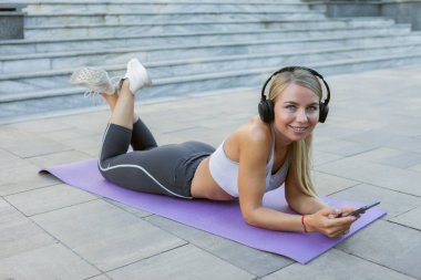 Çekici ince zekalı kadın mindere uzanıp kulaklıklarla müzik dinliyor.