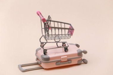 Seyahat ve alışveriş konsepti. Mini plastik seyahat valizi ve bej arka planda süpermarket tramvayı.