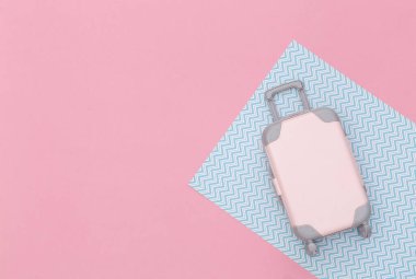 Seyahat konsepti. Pembe pastel arka planda mini plastik bir valiz. Asgari düzeyde. Üst manzara, düz uzanma