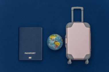 Dümdüz git. Mini plastik seyahat valizi, pasaport, klasik mavi arka planda dünya. Asgari düzeyde. Üst görünüm