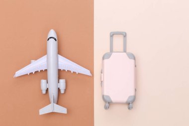 Seyahat minimalizmi. Mini plastik seyahat valizi ve bej rengi kahverengi arka planda uçak. Asgari düzeyde. Üst manzara, düz uzanma