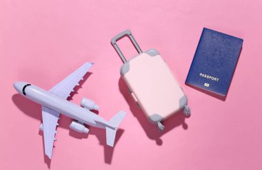 Seyahat minimalizmi. Mini plastik seyahat valizi, pasaport ve arka planda koyu gölgeli bir uçak. Asgari düzeyde. Üst manzara, düz uzanma