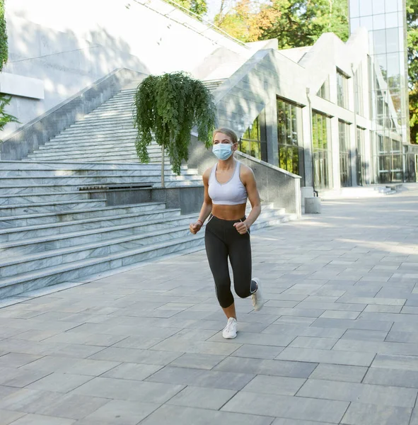 Fit woman in sportswear and medical face mask doing morning jog outdoors. Sports during covid-19 period