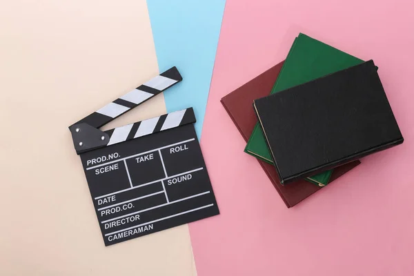 Film clapper board and books on colored pastel background. Movie by book. Cinema industry, entertainment. Top view