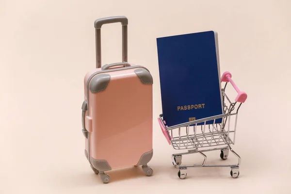 旅行和购物的概念 带有米色背景护照的迷你塑料旅行箱和超市推车 — 图库照片