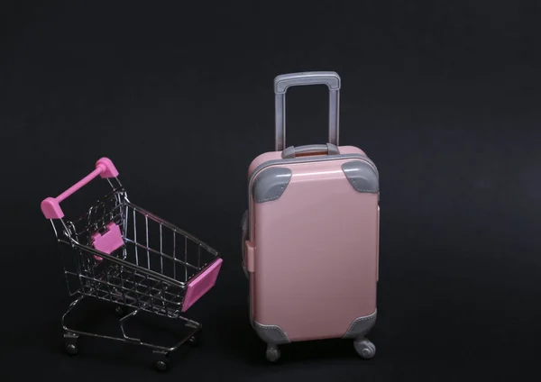 旅行やショッピングのコンセプト 黒を背景にミニプラスチック旅行スーツケースとスーパーマーケットトロリー — ストック写真