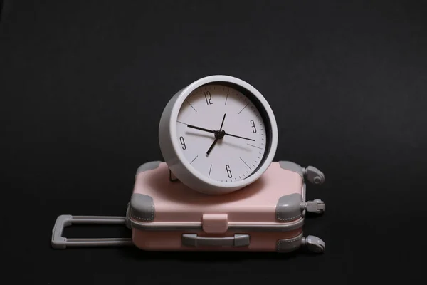 Time to travel. Mini plastic travel suitcase and clock on black background.