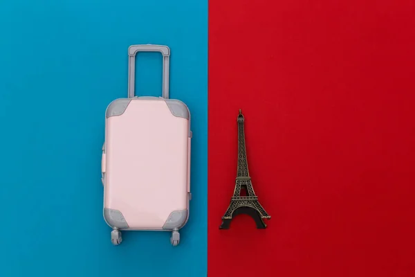 Traveled to Paris. Mini plastic travel suitcase and statuette of the Eiffel Tower on red blue background. Top view. Flat lay