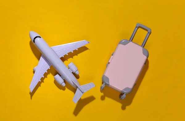 Travel minimalism. Mini plastic travel suitcase and air plane on yellow background with deep shadow. Minimal style. Top view, flat lay