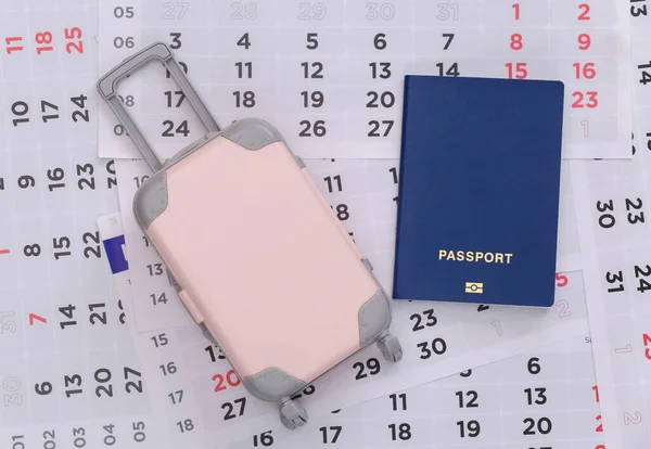 Time to travel. Mini plastic travel suitcase and monthly calendar with passport. Minimal style. Top view. Flat lay
