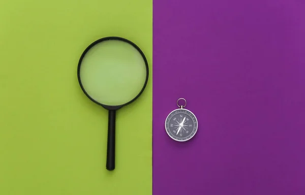 Minimalism travel, adventure flat lay. Compass and magnifier on purple green background. Top view