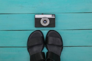 Dişi deri deri sandaletler ve mavi ahşap arka planda retro kamera. Üst görünüm