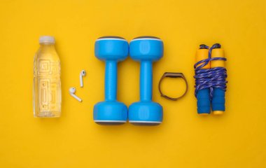 Sarı arka planda spor kıyafetleri, aksesuarlar ve aletlerin düz kompozisyonu vardı. Sağlıklı yaşam tarzı, spor anlayışı. Üst görünüm