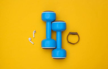 Sarı arka planda spor aletleri (akıllı bilezik ve kablosuz kulaklıklar). Üst görünüm