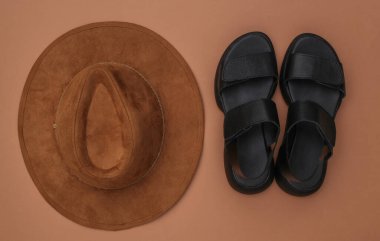 Dişi deri sandaletler ve kahverengi arka planda şapka. Üst görünüm