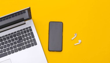 Laptop, akıllı telefon ve sarı arka planda kablosuz kulaklık. Üst görünüm