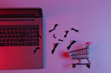 Laptop ve uçan kağıt, mavi neon ışıklı alışveriş arabasıyla yarasaları kesiyor. Cadılar Bayramı teması