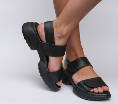 Beyaz arka planda şık deri sandaletler giyen kadın ayakları.