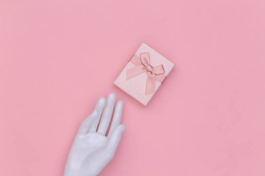 Beyaz manken eli ve pembe arka planda hediye kutusu. Üst görünüm