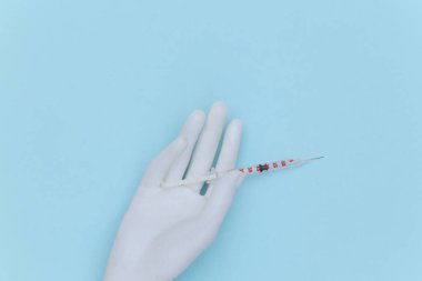 Mavi arka planda beyaz manken elinde şırınga var.