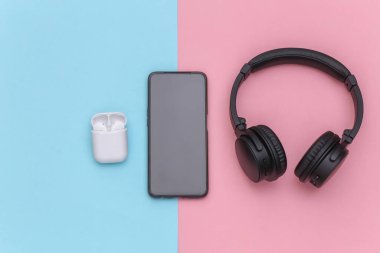 Akıllı pone, kablosuz büyük kulaklıklar ve pembe mavi pastel arka planda şarj kutusu olan küçük kulaklıklar. Üst görünüm